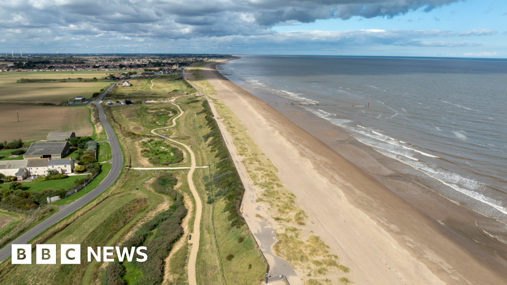 Aerial view of the Lincolnshire coastline showing the restored Sandilands nature reserve beside a long sandy beach. There is a winding footpath, along with dunes and the North Sea on one side and farmland and buildings on the other.