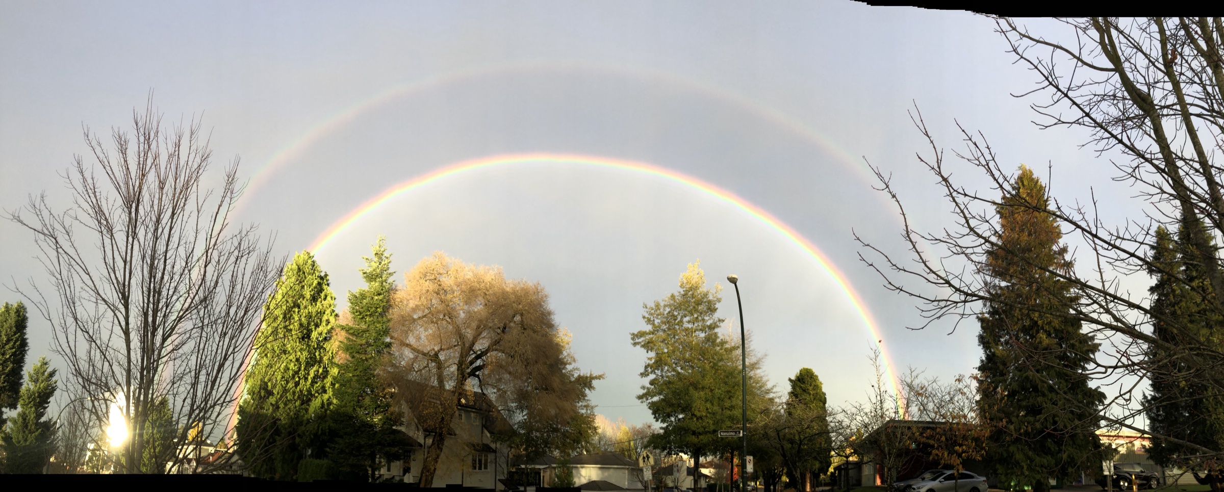 A double rainbow arches over a Vancouver street after rain.